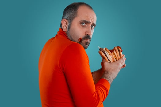Close-up portrait of a middle-aged man with beard, dressed in a red turtleneck, posing with burgers against a blue background. Fast food. photo
