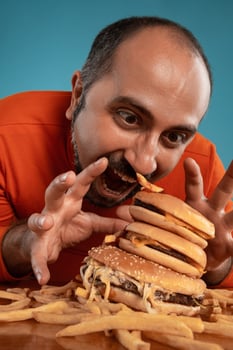 Close-up portrait of a middle-aged man with beard, dressed in a red turtleneck, posing with burgers and french fries. Blue background. Fast food. photo