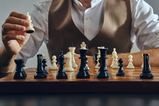 Hands of a man, dressed in a classic brown vest and white shirt siting at a table and playing chess byhimself. Grey background, close-up shot. photo