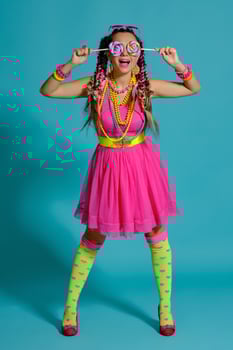 Lovely girl with a multi-colored braids hairstyle and bright make-up, posing in studio against a blue background, holding a lollipop in her hand. photo