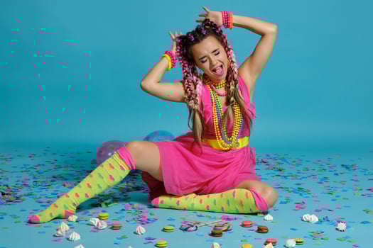 Lovely girl with a multi-colored braids hairstyle and bright make-up, posing in studio with air balloons and confetti against a blue background. photo