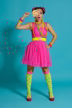 Lovely girl with a multi-colored braids hairstyle and bright make-up, posing in studio against a blue background, holding a lollipop in her hand. photo