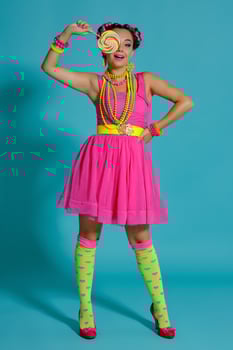 Lovely girl with a multi-colored braids hairstyle and bright make-up, posing in studio against a blue background, holding a lollipop in her hand. photo