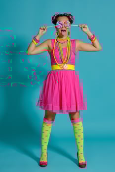 Lovely girl with a multi-colored braids hairstyle and bright make-up, posing in studio against a blue background, holding a lollipop in her hand. photo