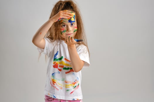 Little girl in white painted t-shirt, with colored face is playing with a sponge soaked in paint. Isolated on white. Close-up. photo