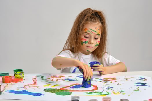 Little girl in white t-shirt sitting at table with whatman and paints, drawing on it, posing with painted face, hands. Isolated on white. Close-up. photo