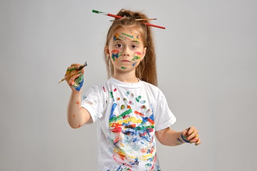 Little girl in white t-shirt, with brushes in her hair is posing standing isolated on white, gesticulating with painted hands and face. Close-up. photo
