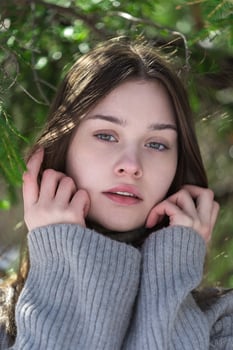 Close-up portrait of Caucasian teenager girl looking at camera, raised hands to face wearing sweater photo