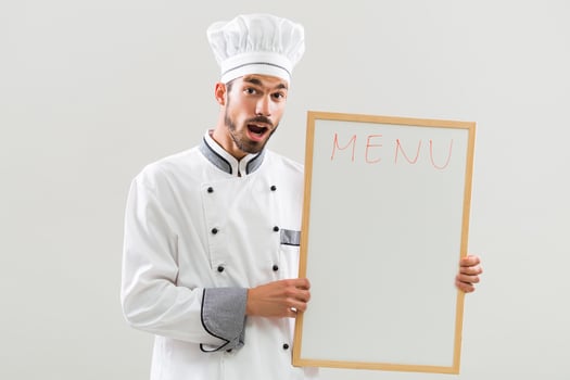 Excited chef is holding whiteboard on gray background photo