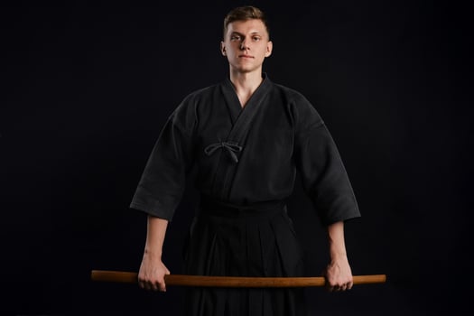 Kendo guru wearing in a traditional japanese kimono is practicing martial art with the shinai bamboo sword against a black studio background. photo