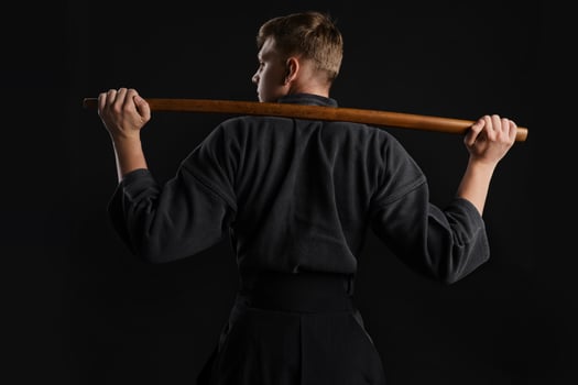 Kendo guru wearing in a traditional japanese kimono is practicing martial art with the shinai bamboo sword against a black studio background. photo