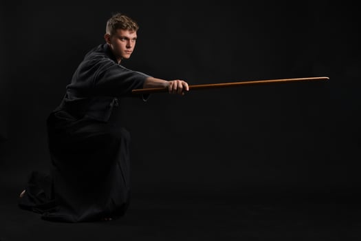 Kendo guru wearing in a traditional japanese kimono is practicing martial art with the shinai bamboo sword against a black studio background. photo