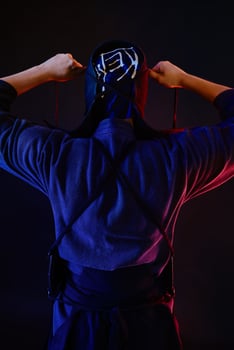 Close up shot, Kendo fighter wearing in an armor and traditional kimono is tying the lacing on his helmet standing back against a black background. photo