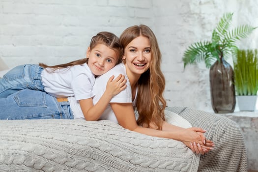 Indoor portrait of a beautiful mother with her charming little daughter posing against bedroom interior. photo