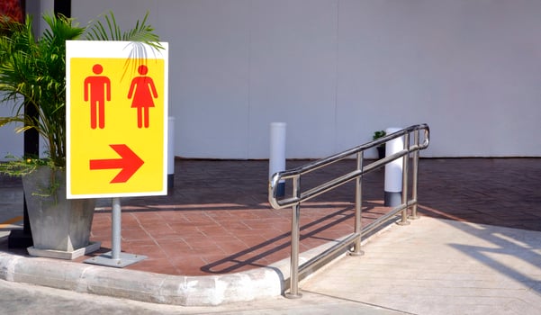 Sunlight on surface of restroom sign on metal pole with stainless steel fence on the different level ground in parking area photo