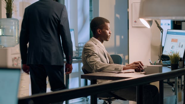 African american employee crosschecking financial figures between clipboard charts and diagrams on computer screen during nightshift. Efficient worker comparing company numbers in office photo