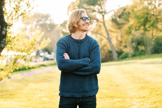 Outdoor portrait of handsome 35 - 40 year old man with red hair, posing in green sunny park, wearing blue pullover and sunglasses photo