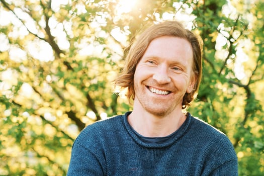 Outdoor portrait of handsome 35 - 40 year old man with red hair, posing in green sunny park, wearing blue pullover photo