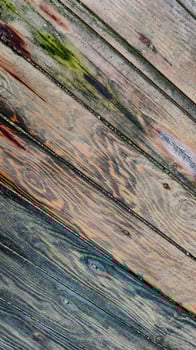 Background of textured wooden surface made of boards with multicolored spots from humidity, diagonal lines, top view, closeup. photo