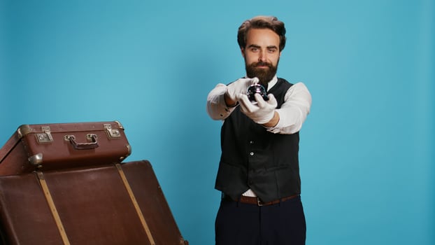 Stylish bellboy with luggage and bell, using to ring for concierge service at hotel in tourism sector. Doorkeeper porter handling trolley bags to help guests, classy elegant occupation. photo