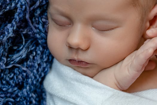 Newborn - baby, face close-up. The sleeping Newborn boy under a white knitted blanket lies on the blue fur. photo