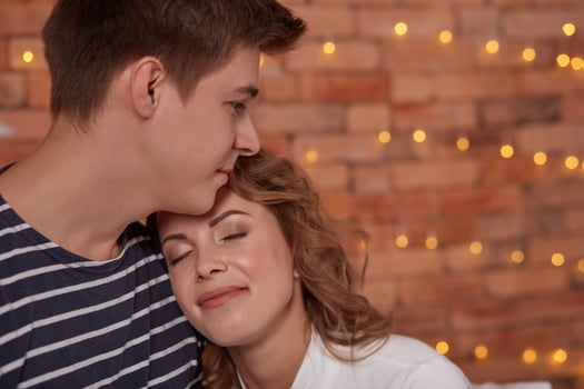 Relation emotions. Young man embracing attractive brunette wife indoor close up photo