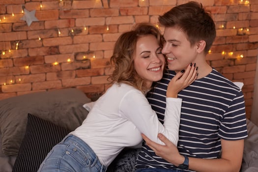 Happy loving couple relaxing on bed at home, young woman touching smiling handsome man face, looking in the eyes. photo