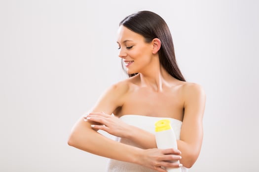 Beautiful woman applying moisturizer on her arm on gray background photo