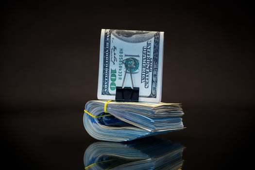 stack of dollar bills collected in an elastic band and a stationery clip photo