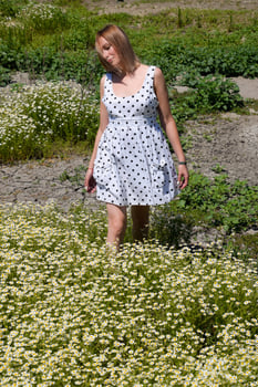 A woman in a white dress with polka dots is on a glade with daisies. Blooming daisies photo