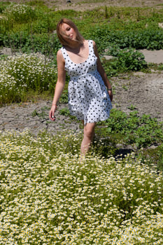 A woman in a white dress with polka dots is on a glade with daisies. Blooming daisies photo