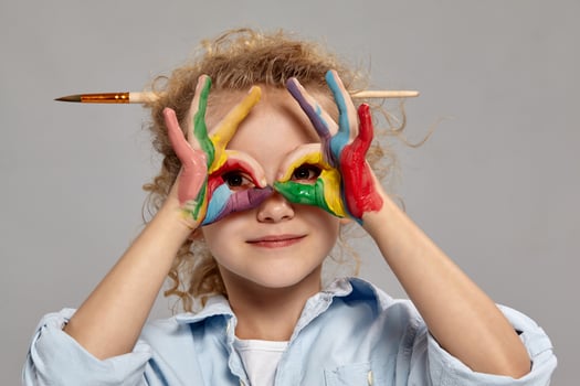 Beautiful little girl with a painted hands is posing on a gray background. photo