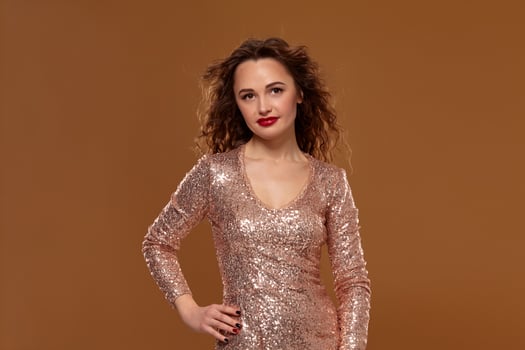 Portrait of young caucasian female in golden cocktail dress looking into the camera on brown background photo