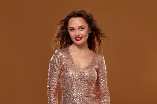 Portrait of young caucasian female in golden cocktail dress looking into the camera on brown background photo