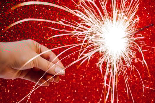 New Year celebration. Womans hand holds bright sparkler on red background. Christmas night. Bright sparks of fire and bokeh. photo