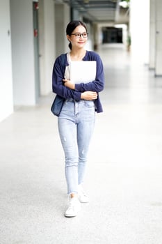 Asian young female student in casual cloth holding a laptop and walk on corridor of school building background. Asian school concept. photo