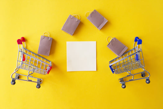 Two mini shopping cart with small craft bags and blank white paper for lettering or shopping list on yellow background. photo