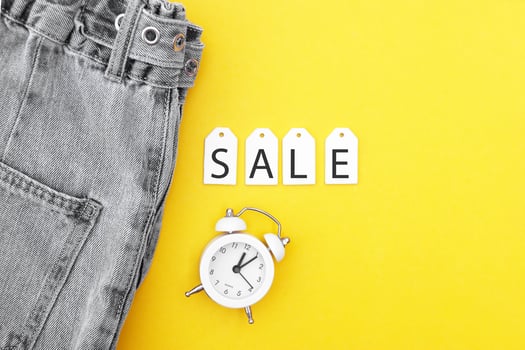 Flat lay, detail of black jeans, white labels and inscription Sale on yellow background. photo