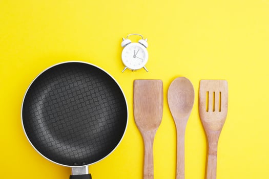 A non-stick skillet, a set of bamboo crockery and a white vintage clock on a bright yellow background. photo