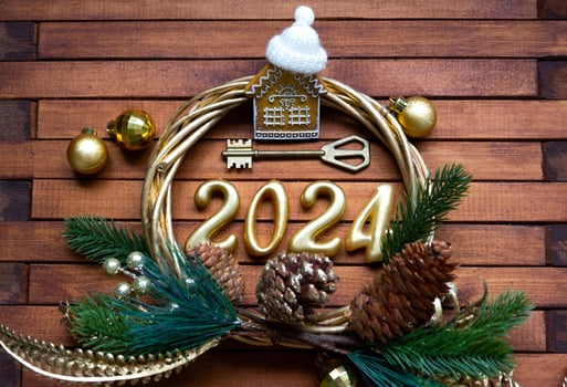 House key with keychain cottage on festive brown wooden background with stars, lights of garlands. New Year 2024 wooden letters, greeting card. Purchase, construction, relocation, mortgage, insurance photo