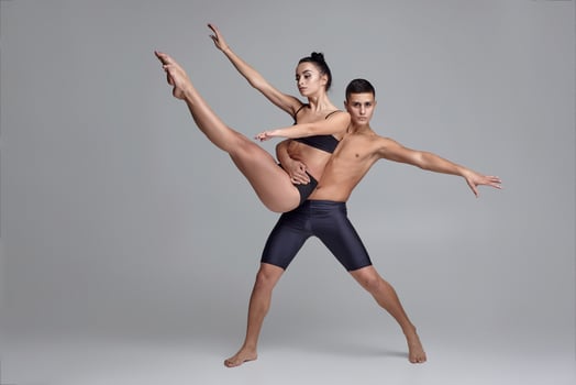 The couple of a young modern ballet dancers in black suits are posing over a gray studio background. photo