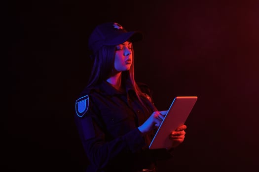 Close-up portrait of a female police officer posing for the camera against a black background with red and blue backlighting. photo