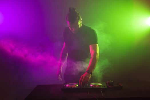DJ at work mixing sound on her decks at a party or night club with colourful smoke light background photo