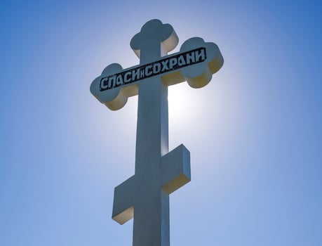 Orthodox cross against the blue sky and the sun. Cross in the ba photo