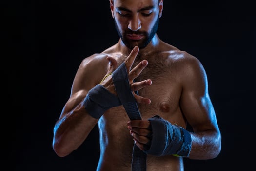 Boxer preparing her gloves for a fight. Photo of muscular man strapping up hands on black background.
