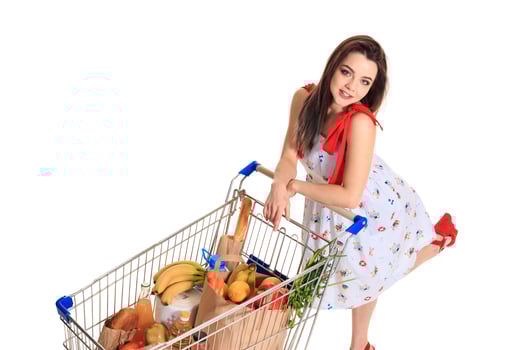 High angle view of girl smiling at camera while pushing a shopping cart full with groceries isolated on white background. photo