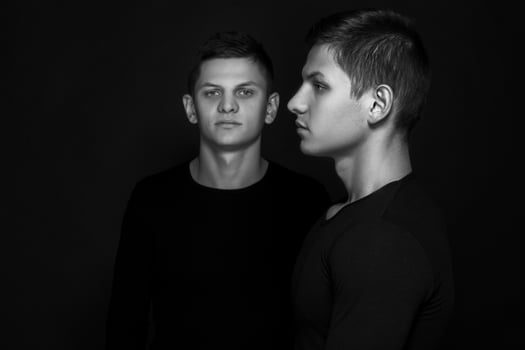Two attractive positive young twin brothers standing dressed in photo