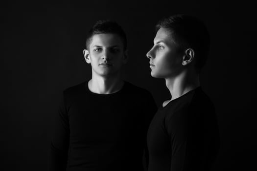 Two attractive positive young twin brothers standing dressed in photo