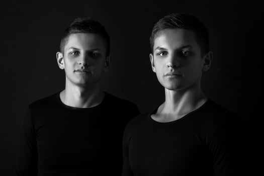 Two attractive positive young twin brothers standing dressed in photo