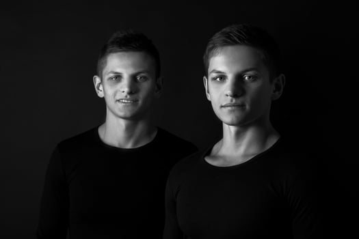 Two attractive positive young twin brothers standing dressed in photo